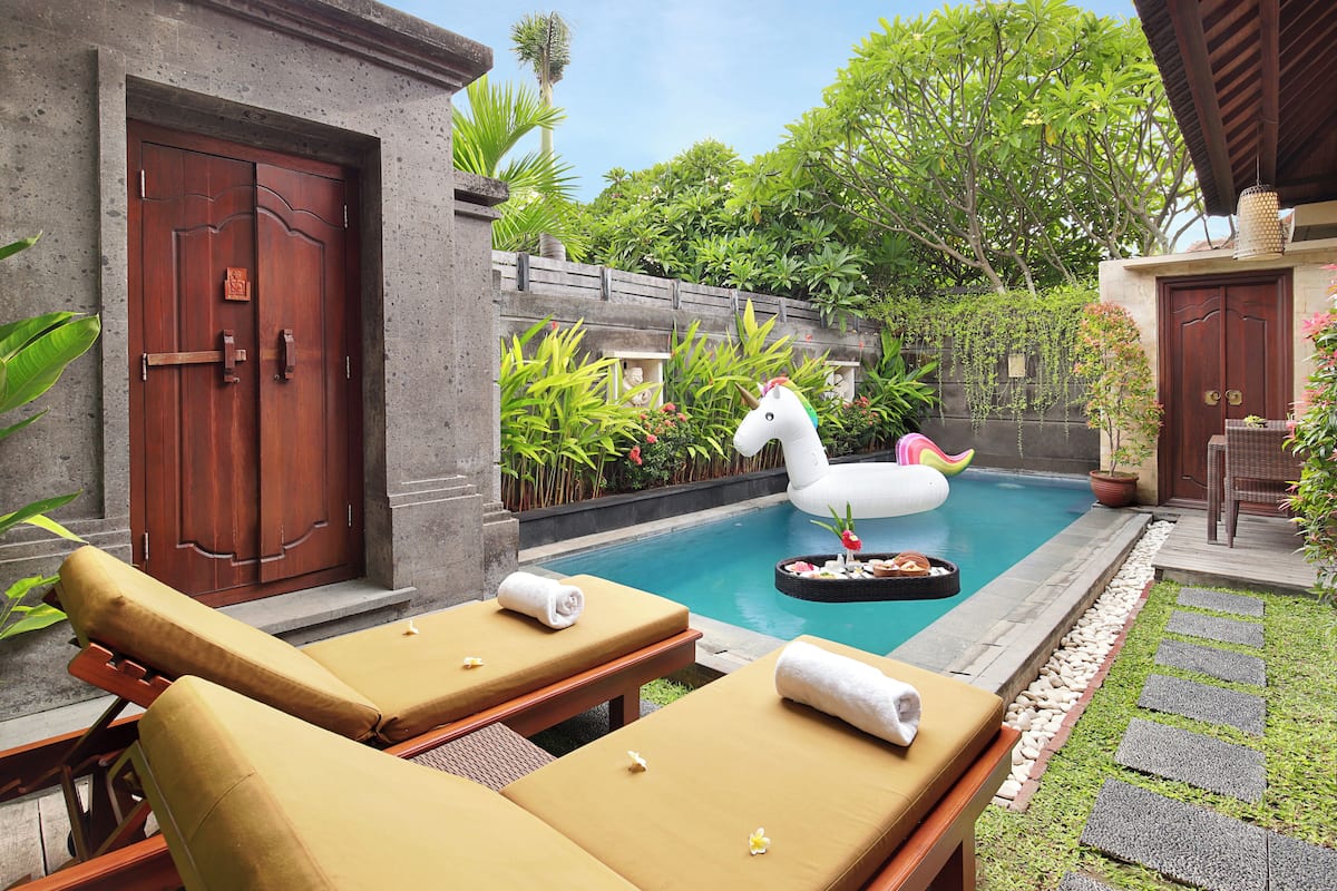 A pool area with lounge chairs, a swan float, and a stone wall with greenery.