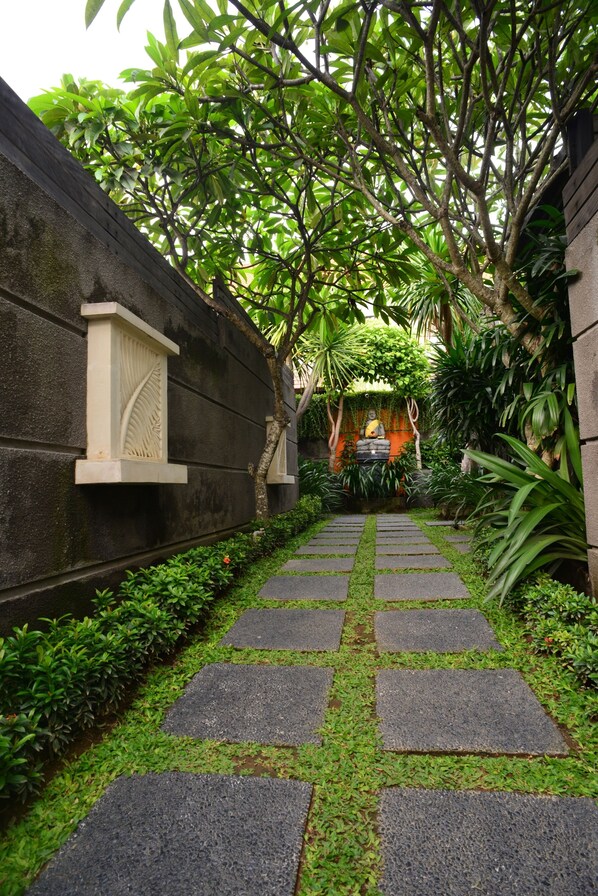 A stone pathway leading to a traditional building with a Buddha statue, surrounded by lush greenery. - Nyuh Bali Luxury Villas (Seminyak)