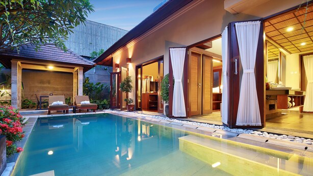 A swimming pool with a clear blue water surface, surrounded by a wooden deck and a covered outdoor seating area. - Nyuh Bali Luxury Villas (Seminyak)