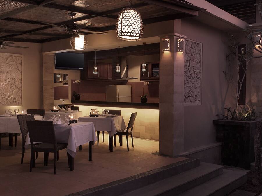 A dining area with tables set for two, overhead pendant lighting, and a modern kitchen in the background.