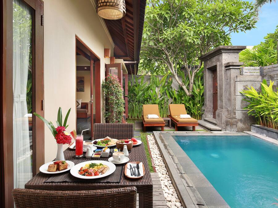 Comedor con vista a la piscina, con una mesa dispuesta con platos, un jarrón de flores y una bebida.