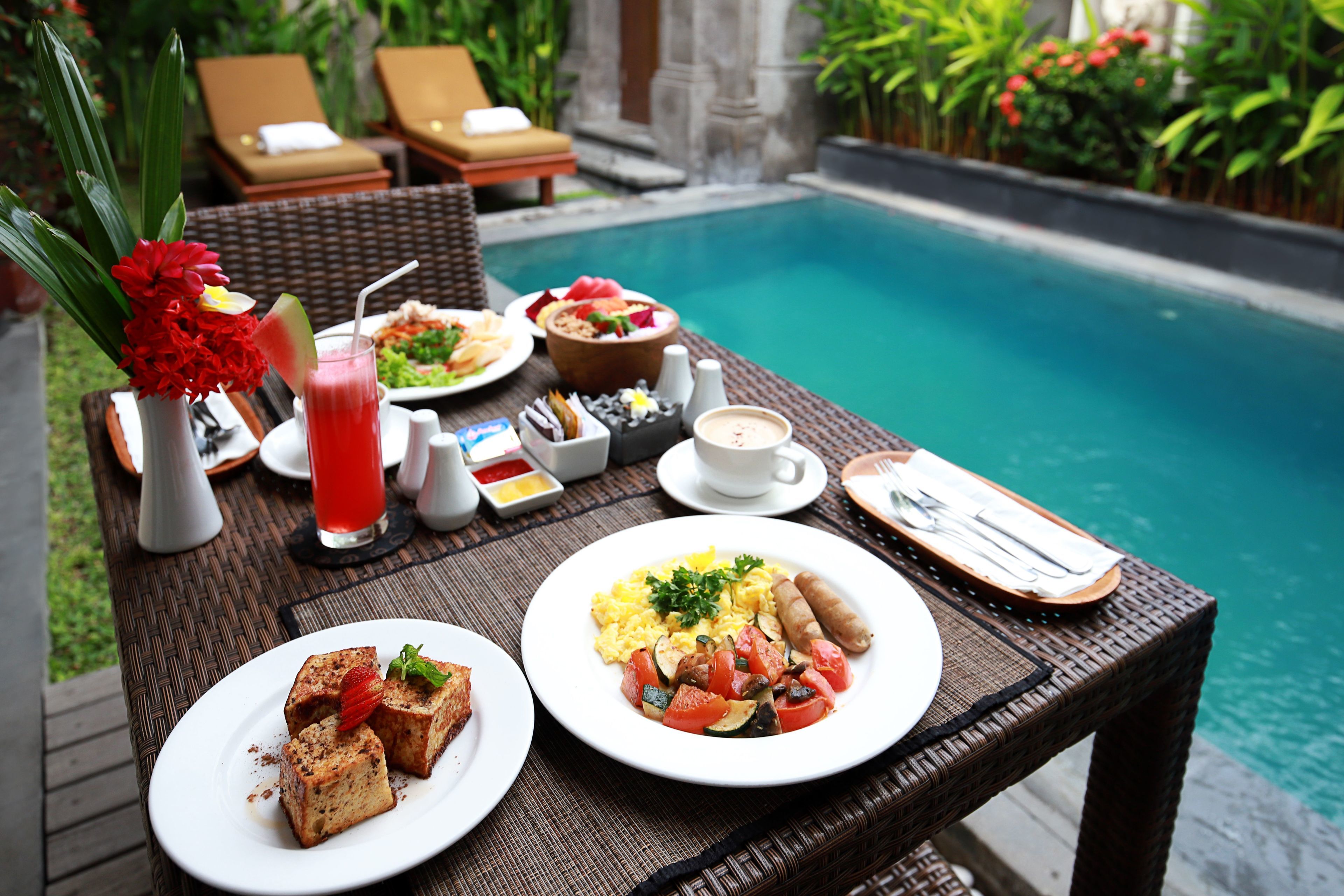 Une table à manger avec des aliments pour le petit-déjeuner, et une piscine en arrière-plan.