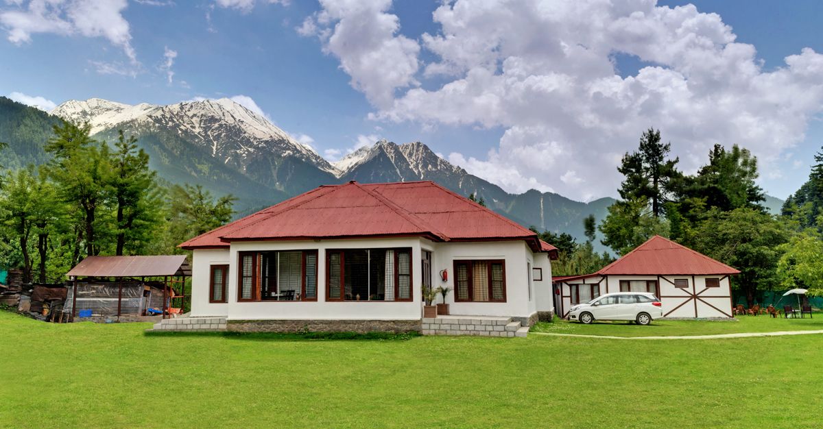 A two-story building with a red roof, surrounded by a well-maintained lawn and trees, with a mountain range in the background.
