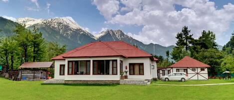 A two-story building with a red roof, surrounded by a well-maintained lawn and trees, with a mountain range in the background.