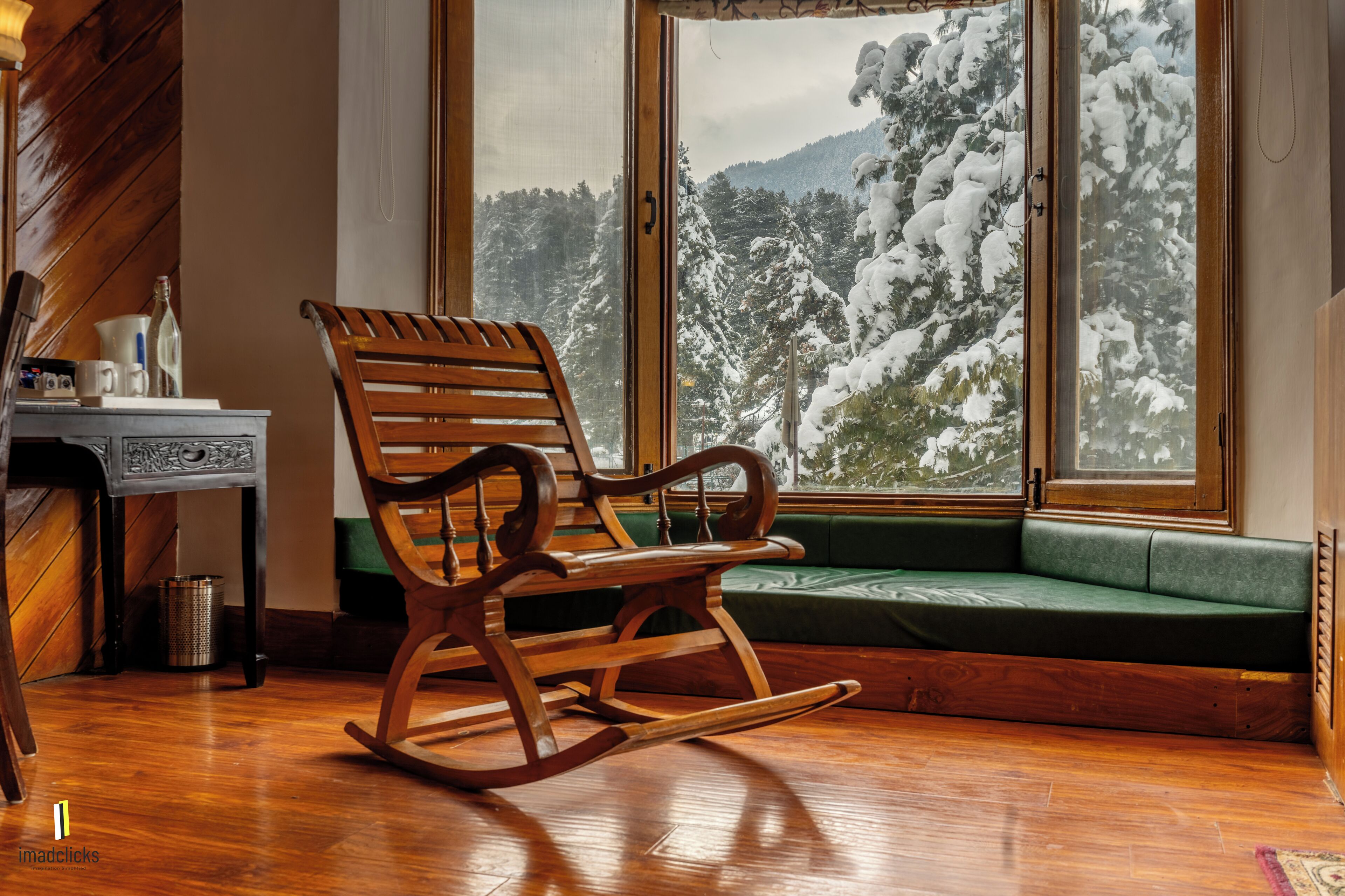 A wooden rocking chair in a room with a large window overlooking a snowy landscape.