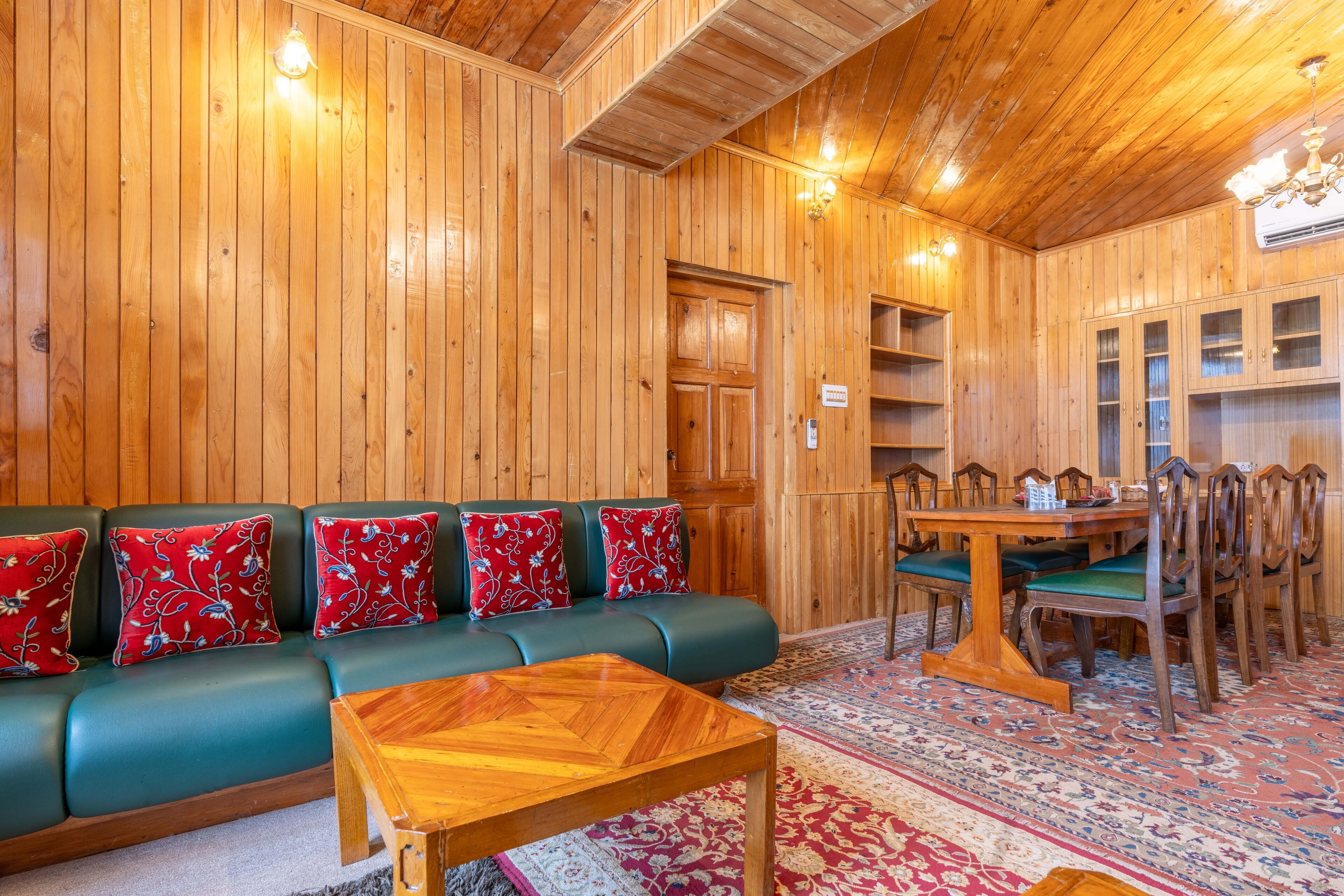 A wooden interior with a green sofa, wooden dining table, and chairs.