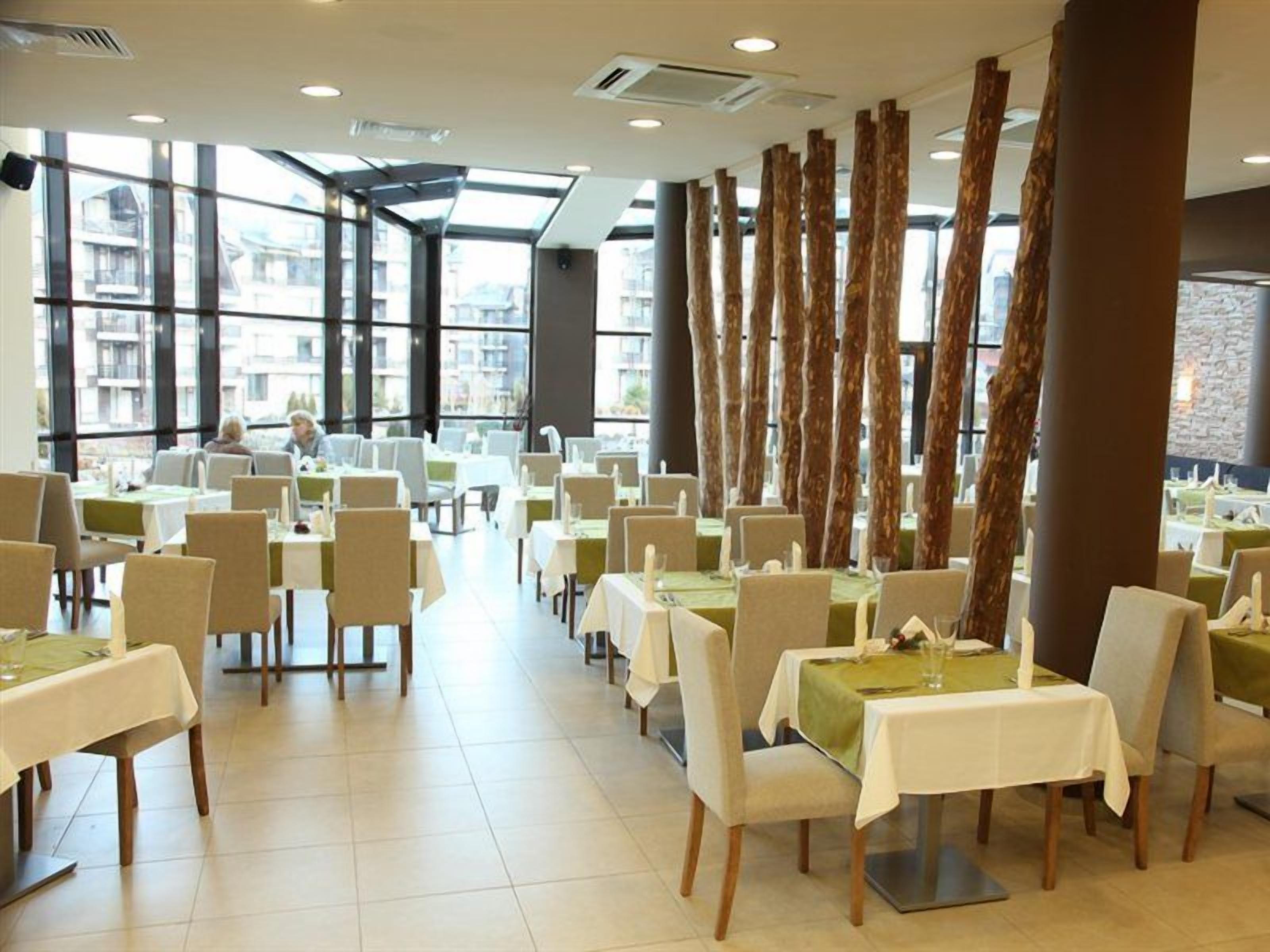 A restaurant with multiple tables and chairs, large windows, and a view of buildings outside.