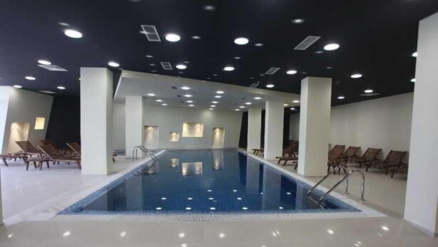 En stor indendørs swimmingpool med flere baner, omgivet af liggestole og et loft med indbygget belysning.