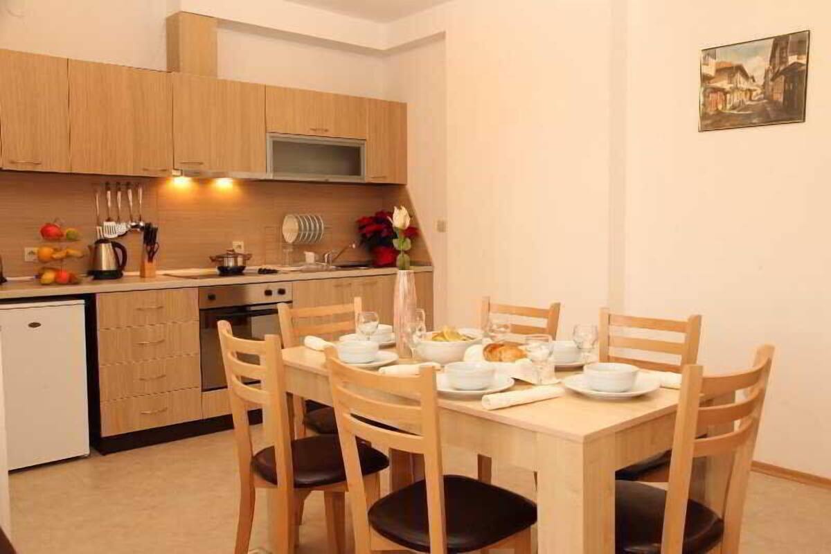 A compact kitchen with wooden cabinets, a dining table set for four, and a small refrigerator.