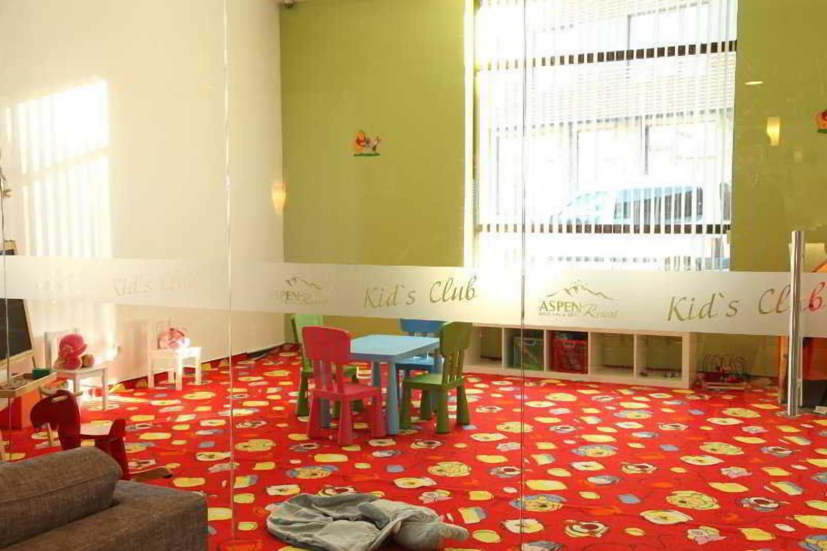 A children's play area with a red carpet, colorful chairs, and a white table.