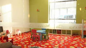 A children's play area with a red carpet, colorful chairs, and a white table.