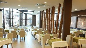 En restaurant med flere borde og stole, store vinduer og en stenvæg i baggrunden.
