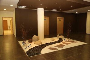 A lobby with a central rug featuring a rock garden design, two wooden doors, and a pillar. - Aspen Resort Golf, Ski & Spa (Razlog)