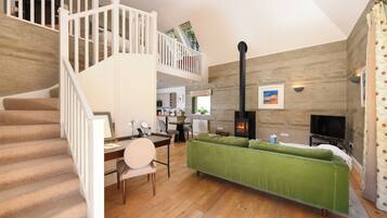 Amplia sala de estar con una escalera, un sofá verde, una chimenea y un televisor.