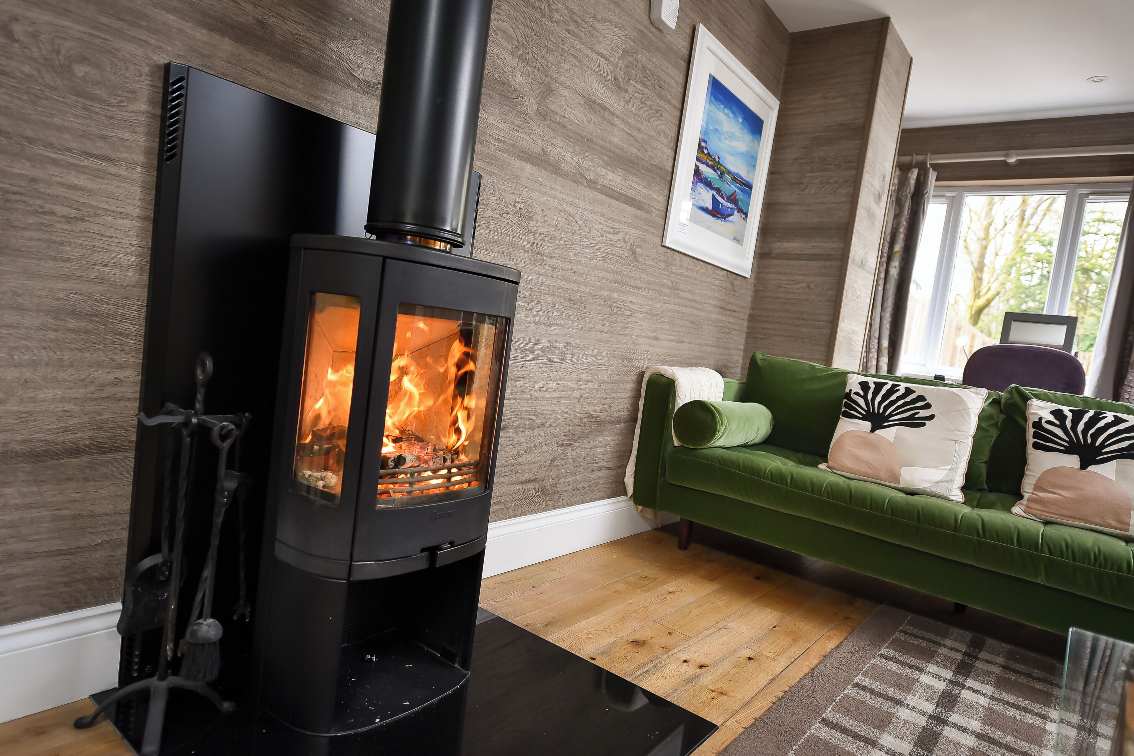 A modern living room with a black wood-burning stove, a green sofa, and a wooden floor.
