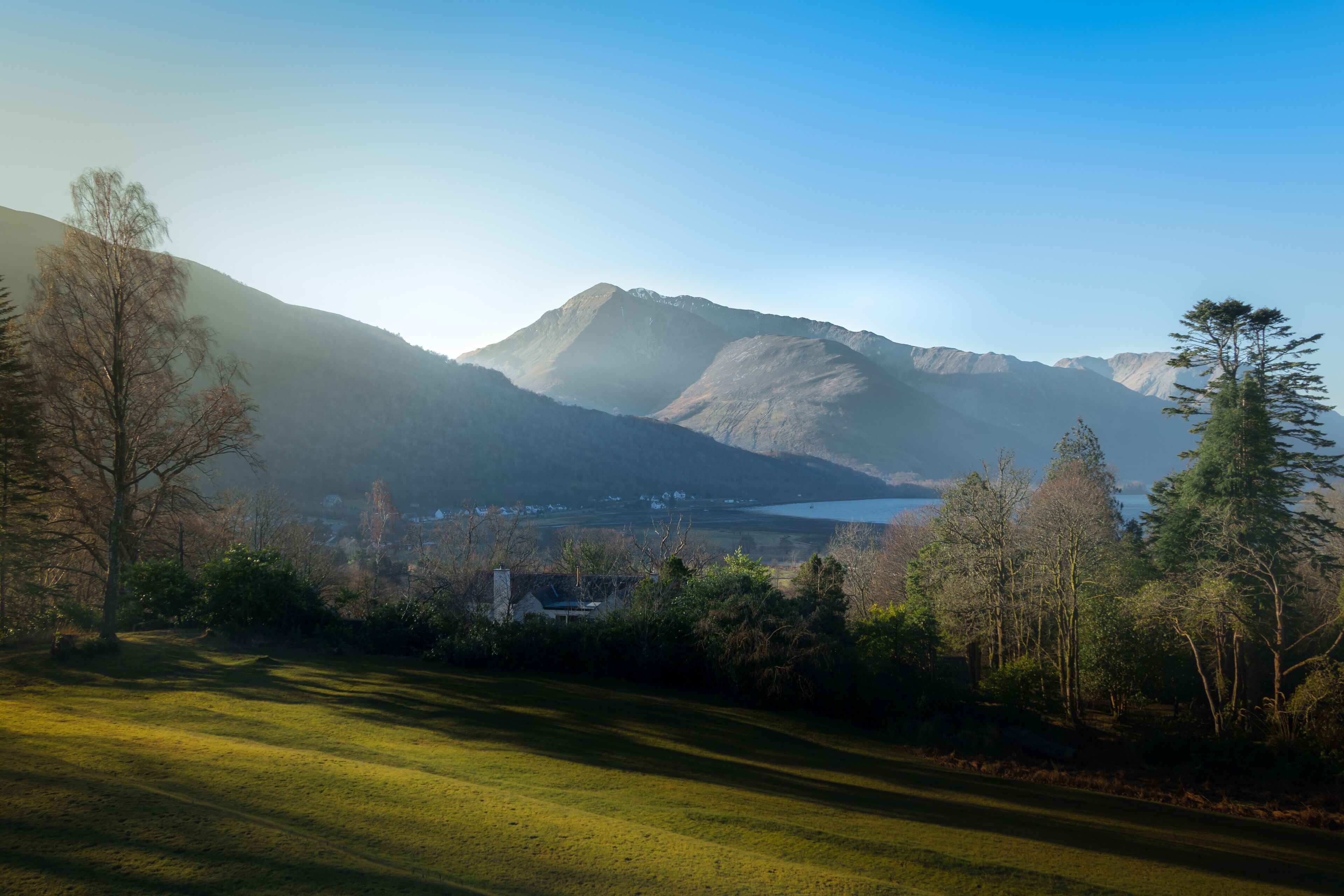 A mountainous landscape with a lake and a small building in the valley.