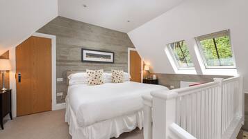 A bedroom with a large bed, a wooden accent wall, two bedside lamps, and a window with a view of greenery.