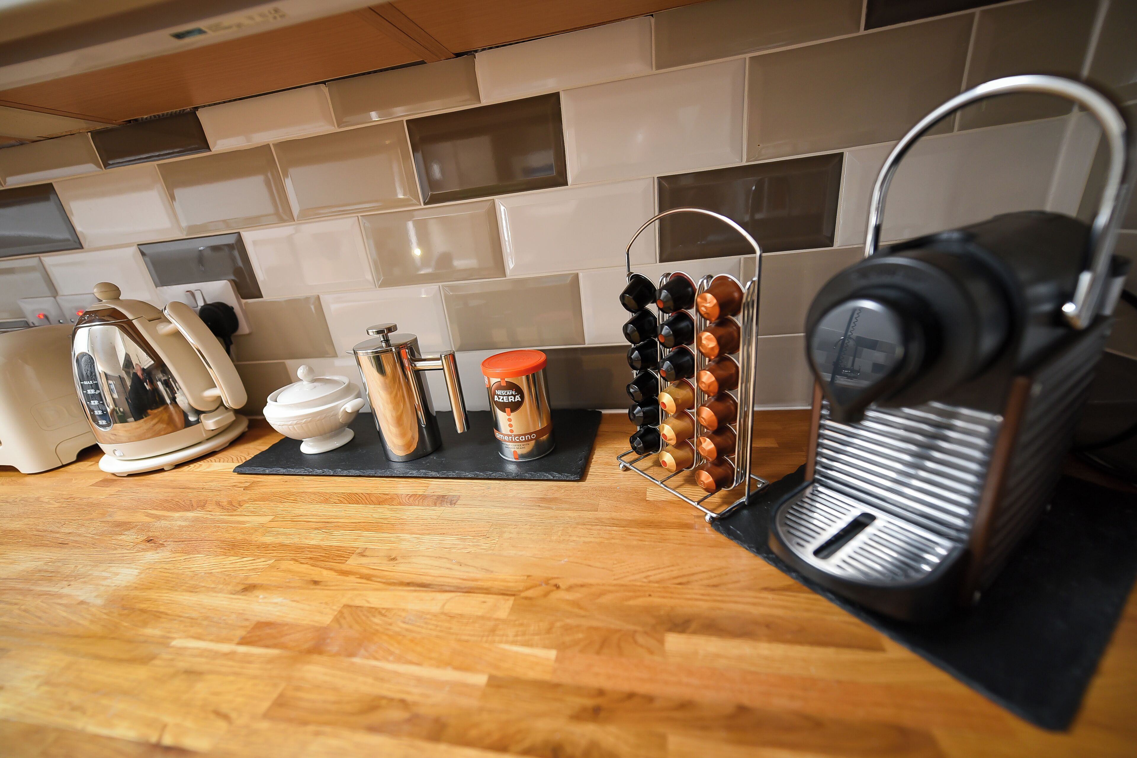 Una cocina con cafetera, hervidor, molinillo de café y un soporte para tazas.