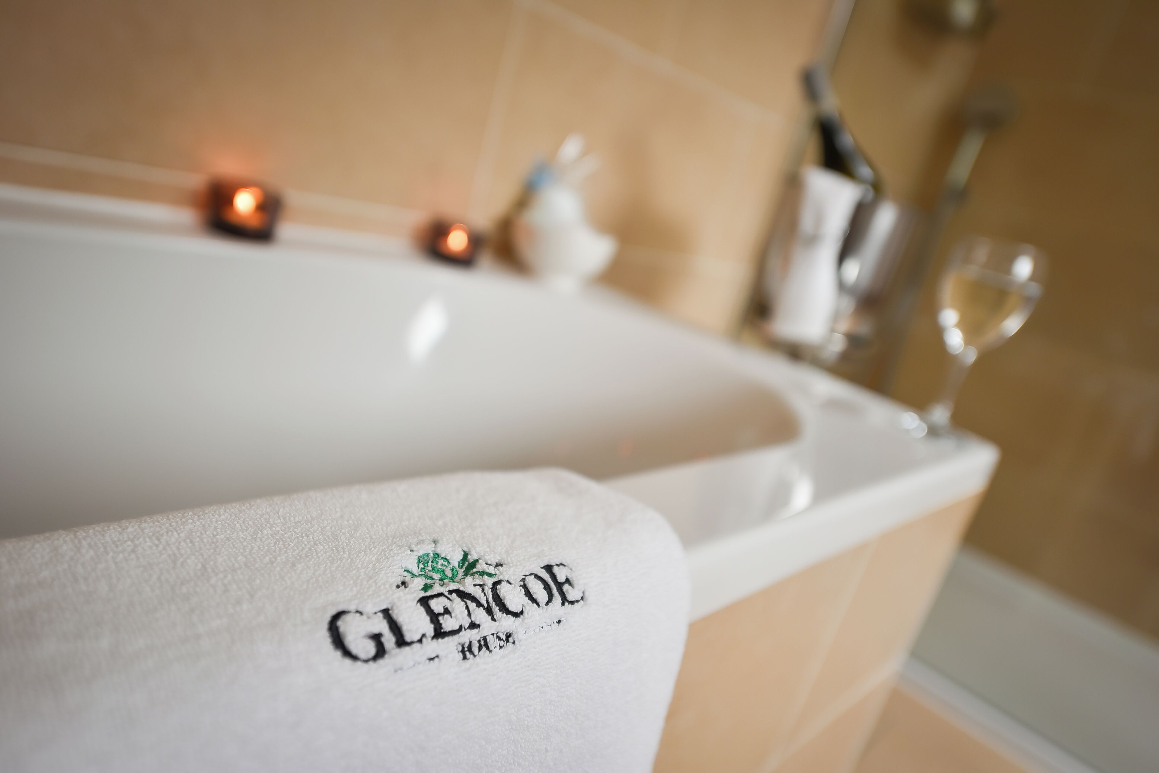 Ett badkar med en handduk där det står "GLENCOE HOTEL", samt en vinflaska och ett vinglas bredvid.