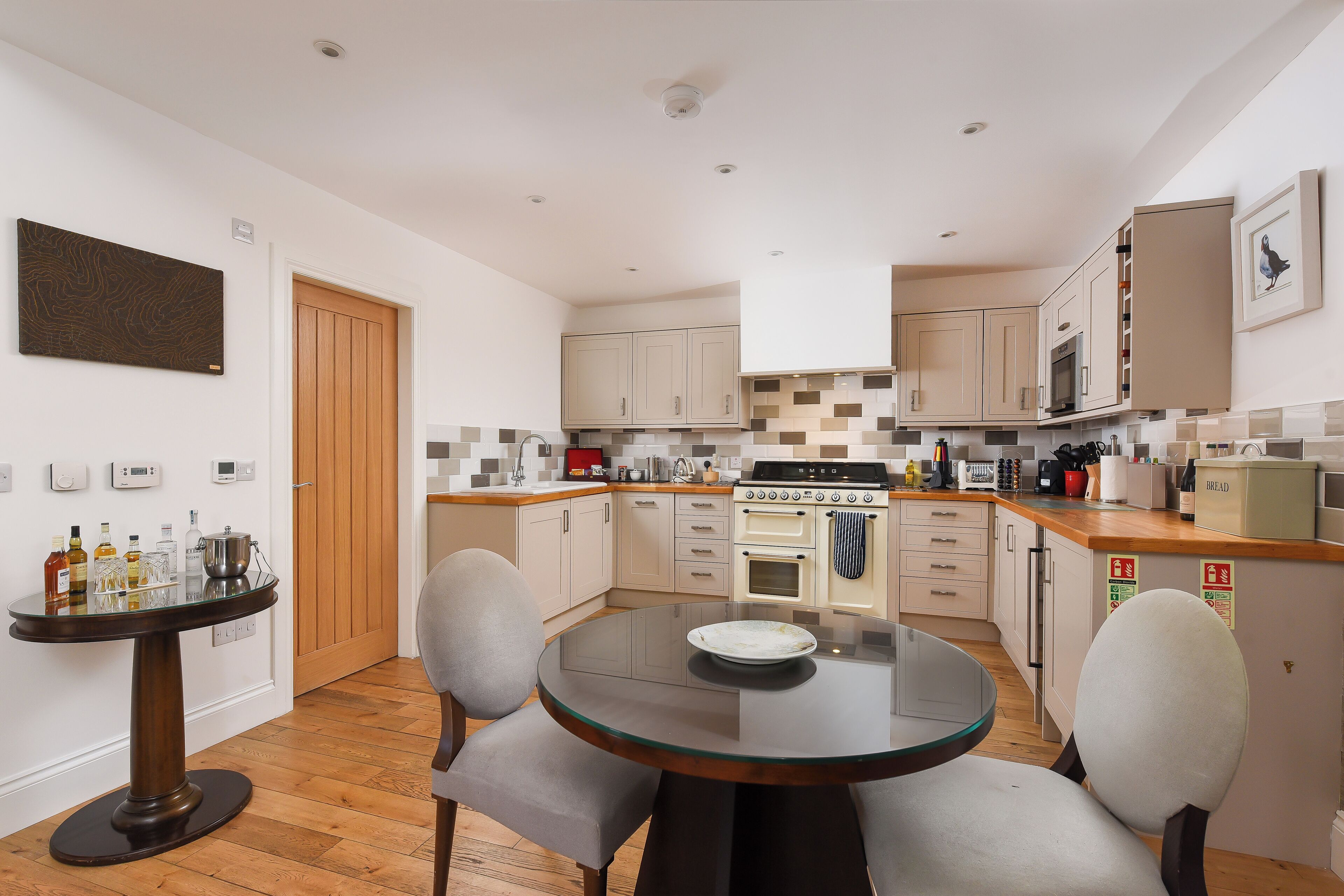 A compact kitchen with a dining area, featuring a round glass table, two chairs, and a wooden floor.
