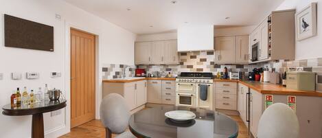 A compact kitchen with a dining area, featuring a round glass table, two chairs, and a wooden floor.
