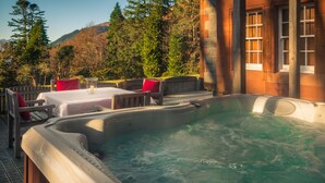 A hot tub with a wooden deck, outdoor seating, and a mountain backdrop.