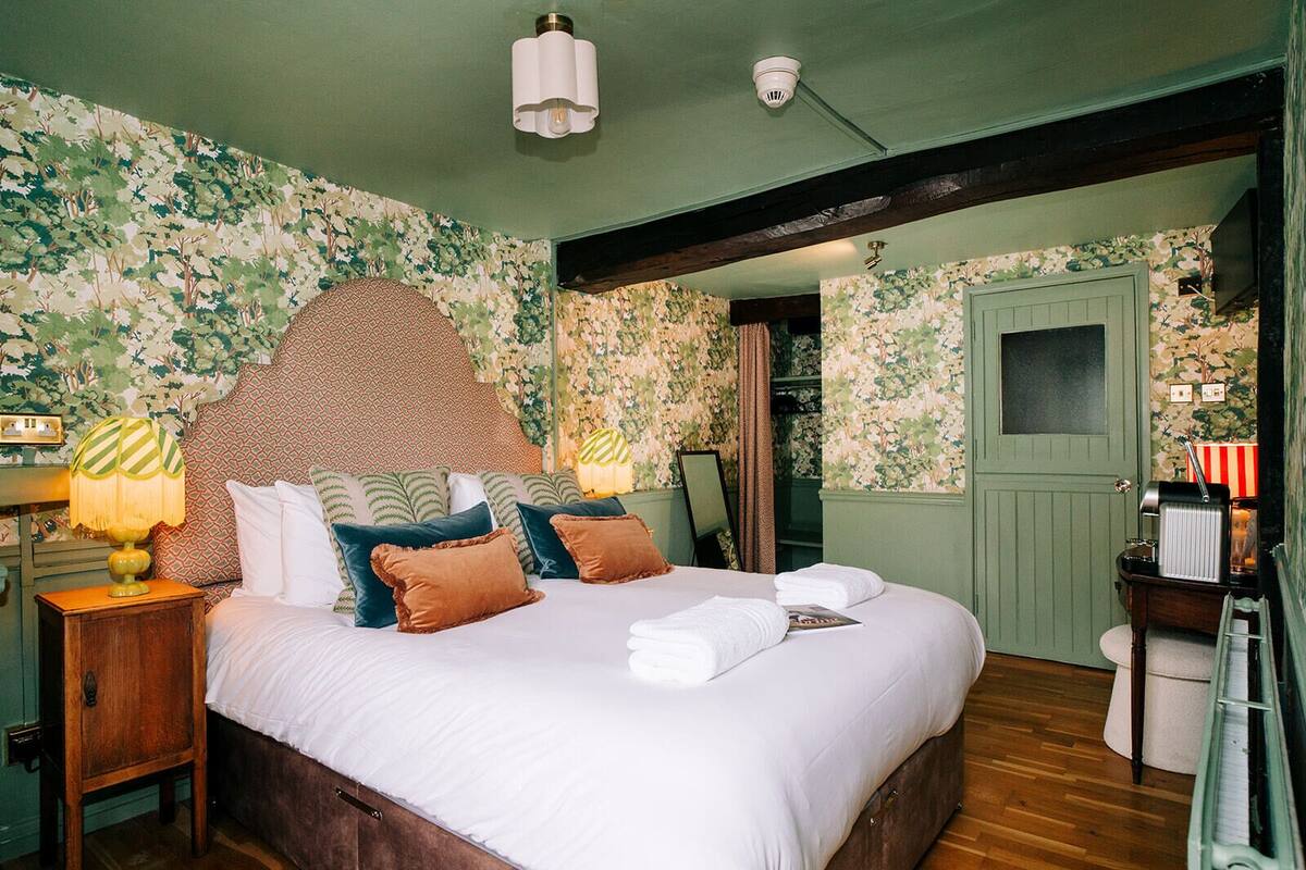 A bedroom with a large bed, a nightstand with a lamp, a mirror, and a dresser with a radio.