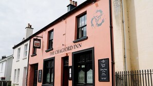 Un edificio con un letrero que dice 'The Chagford Inn' y un cartel negro con el horario de atención.