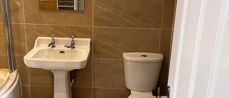 Ein Badezimmer mit einem Standwaschbecken, einer Toilette und einem Spiegel über dem Waschbecken.