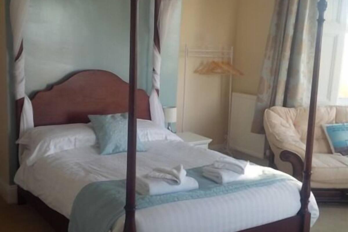 A four-poster bed with white linens, a wooden headboard, and a blue accent pillow.