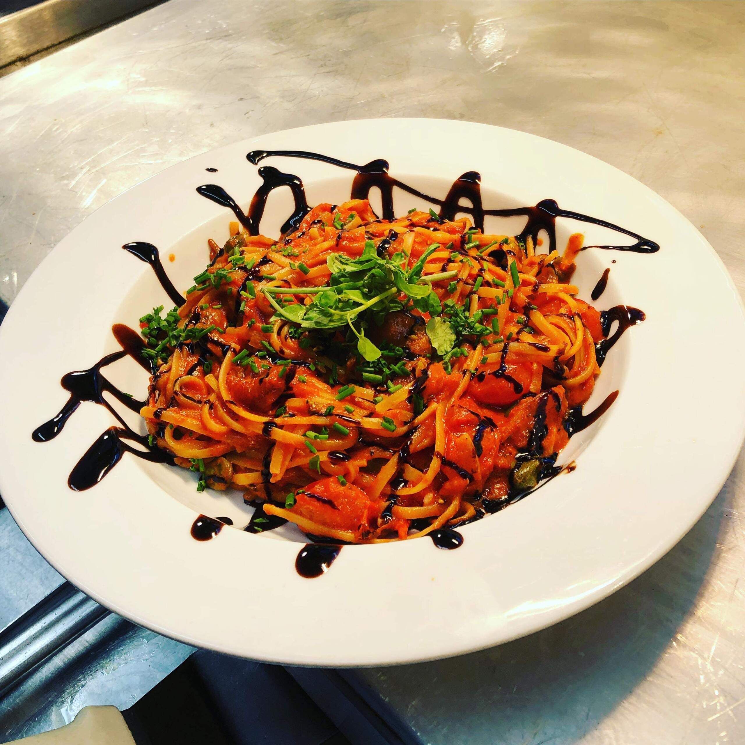 A white plate with a dish of carrots and greens, garnished with a dark sauce.