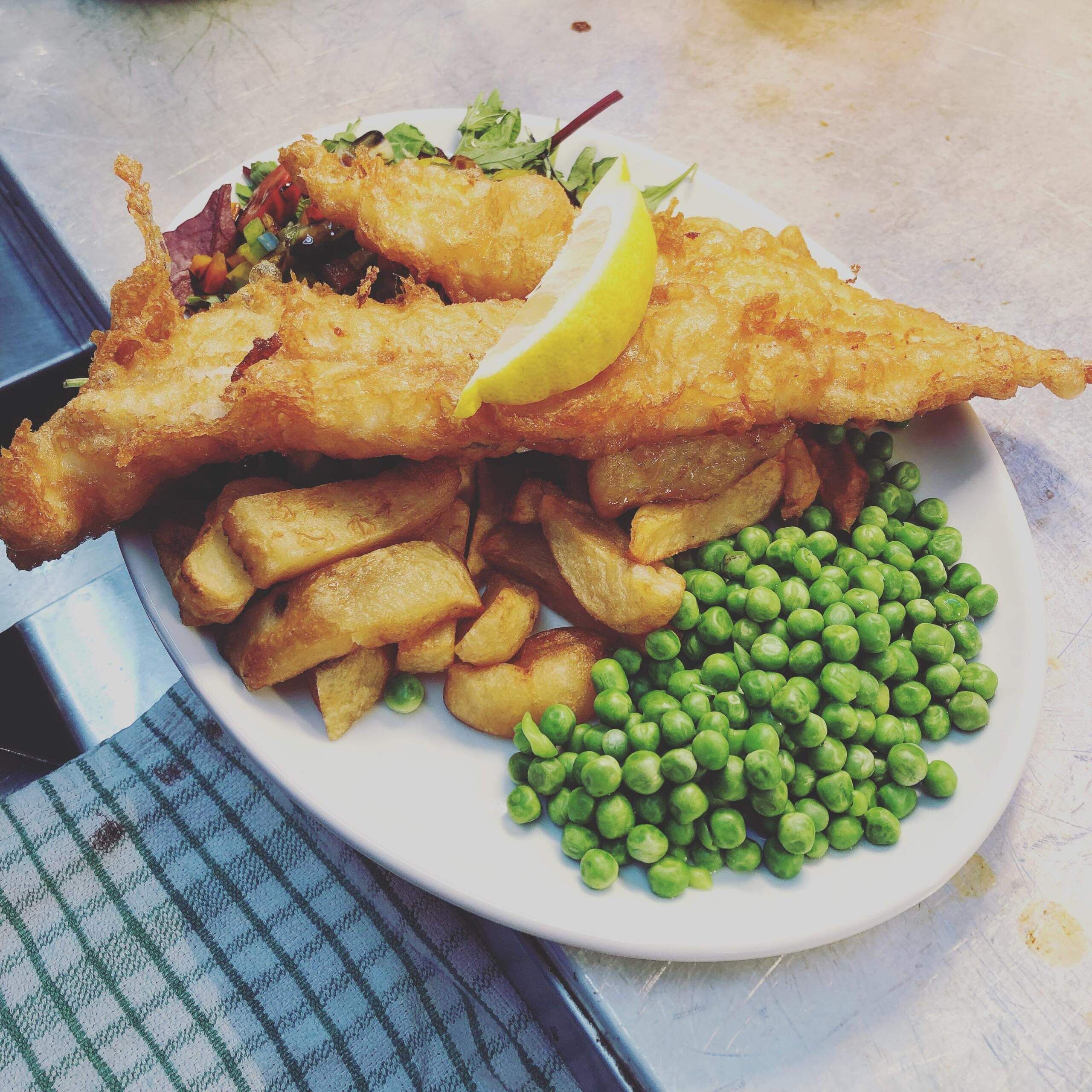 A plate of fish and chips with peas and a lemon wedge.