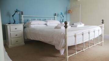 A neatly made bed with white bedding and a metal frame, a bedside table with a lamp, and a wall-mounted drying rack.