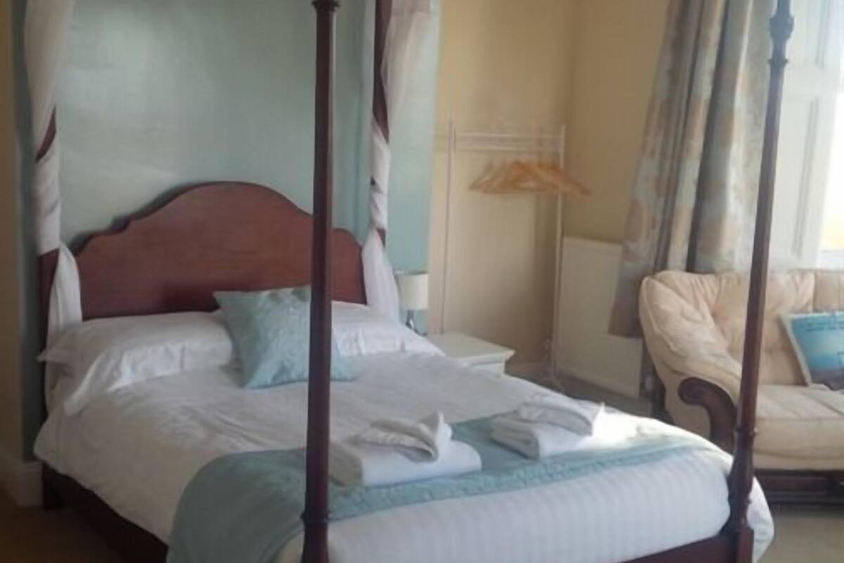 A four-poster bed with white linens, a wooden headboard, and a blue throw blanket.