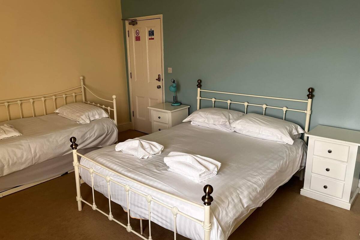 A room with two single beds, each with a nightstand and a drawer. There is a door with a sign above it.