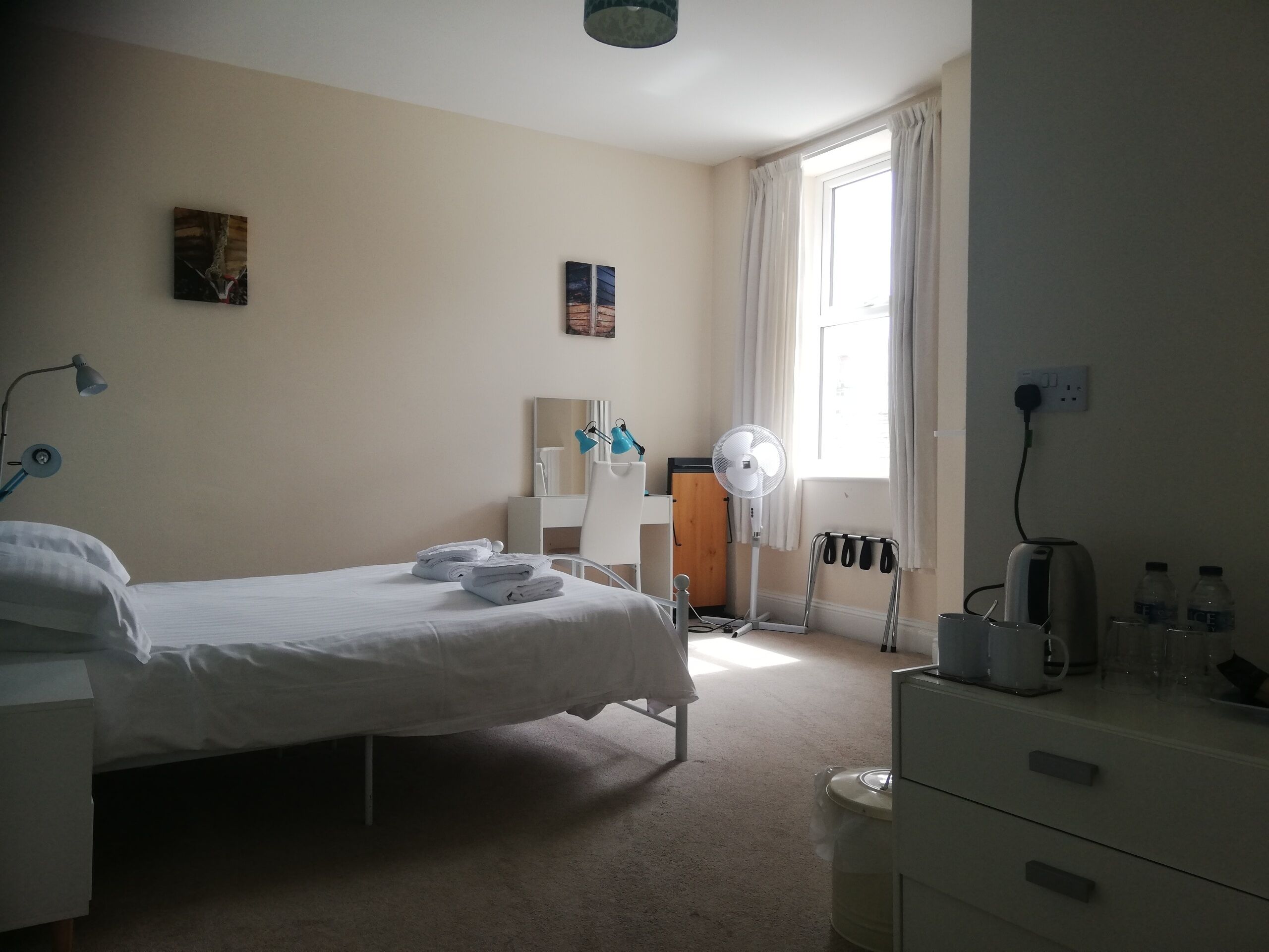 Habitación de hotel con cama, mesita de noche, lámpara, ventilador y vista al exterior por una ventana.