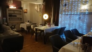 Interno di un ristorante con pavimento in legno, tavoli apparecchiati per la cena e illuminazione decorativa.