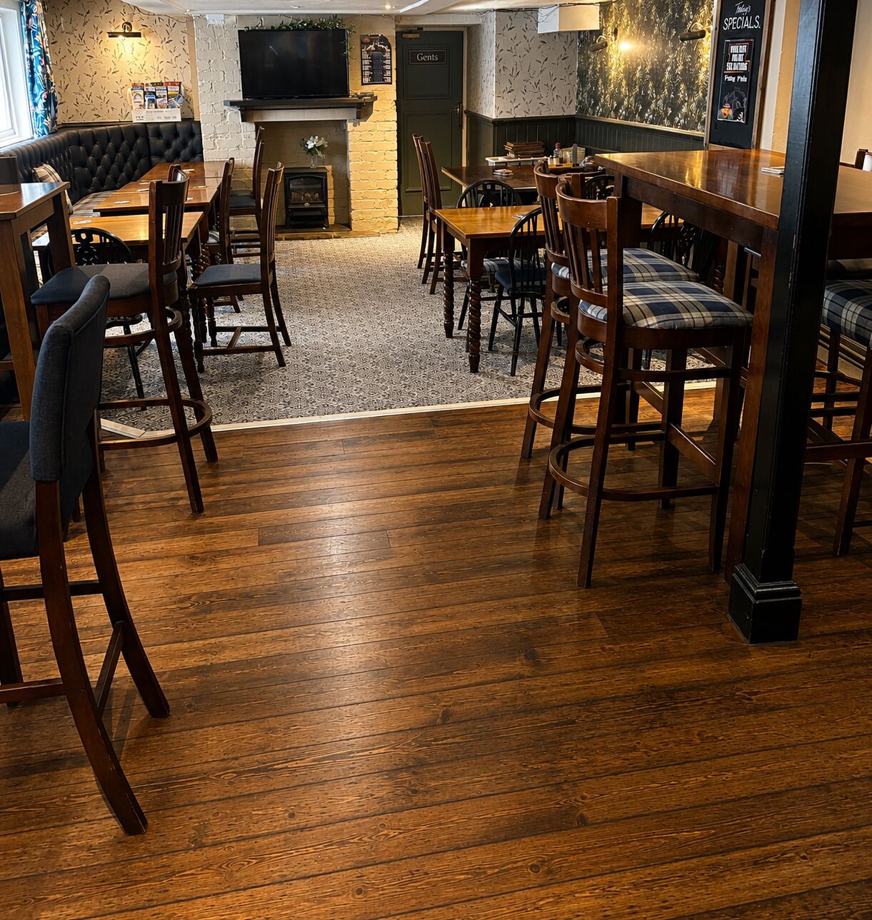 A restaurant with wooden flooring, a fireplace, and a television mounted on the wall.