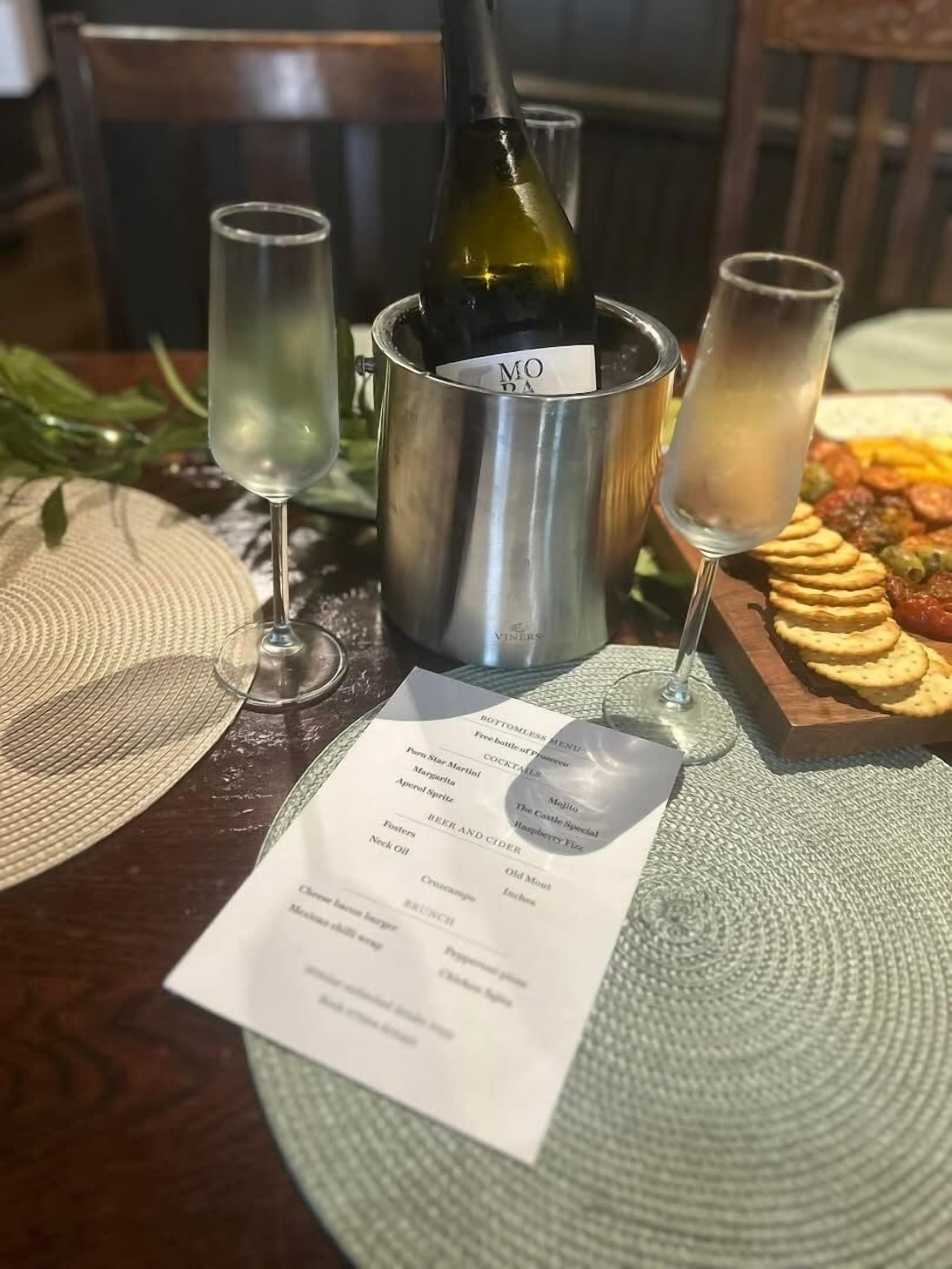 A table with a bottle of wine, two glasses, a menu, and a plate of food.