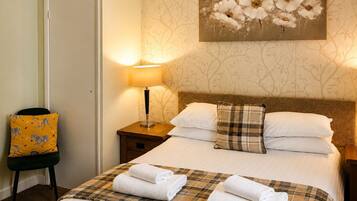 A hotel room with a bed, a nightstand with a lamp, a chair with a zebra-patterned cushion, and a wall with a floral painting.