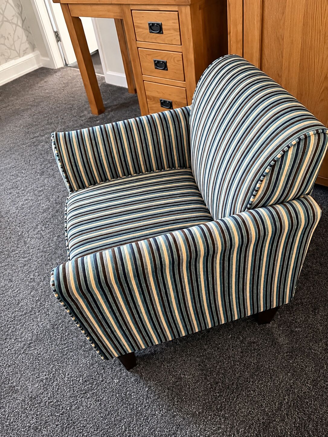 Un sillón a rayas con una mesita de madera y un aparador al fondo.