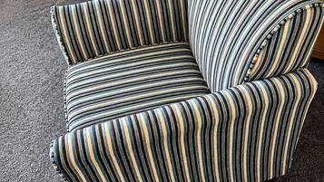 Un sillón a rayas con una mesita de madera y un aparador al fondo.