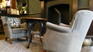 Een woonkamer met twee fauteuils, een kleine ronde tafel en een open haard.