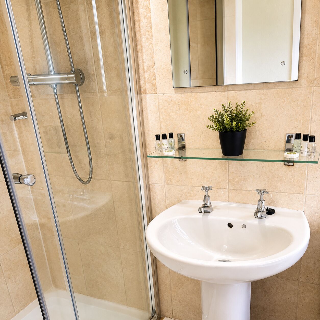 Un baño con cabina de ducha de vidrio, un lavabo blanco y un espejo encima.