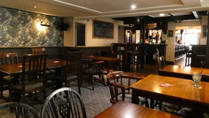 Een restaurant met houten tafels en stoelen, een krijtbordmenu en een bar.