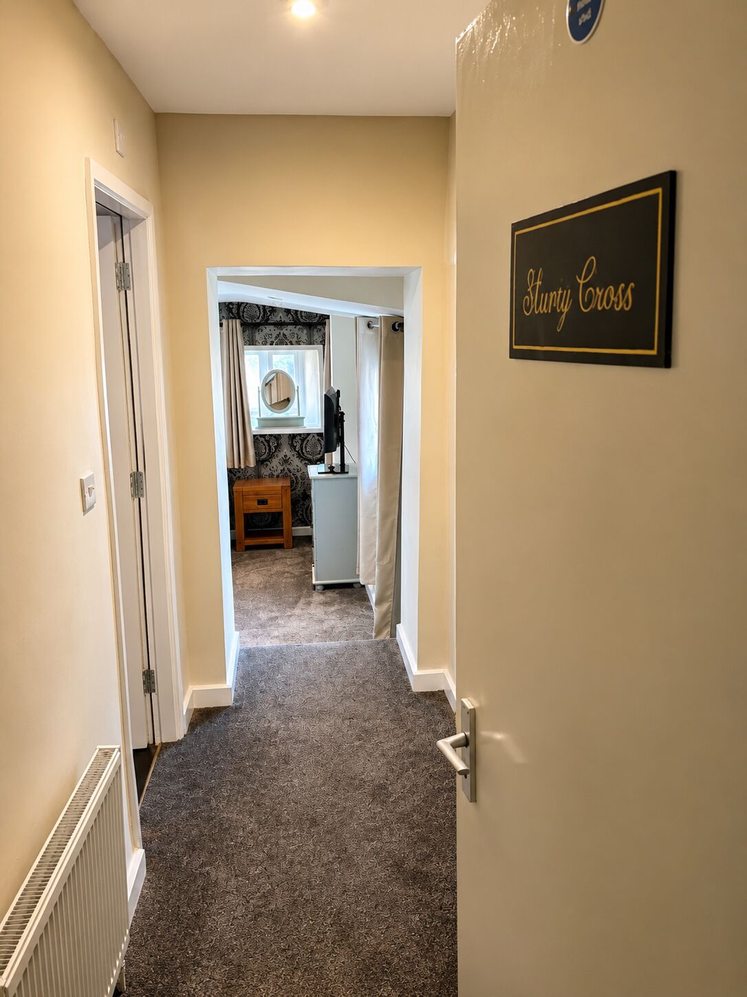 A hallway leading to a bathroom with a vanity, a towel rack, and a sign that reads 'Sturdy Cross'.