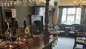 Een bar met verschillende biertappen, een open haard en een zithoek met een bank en stoelen.