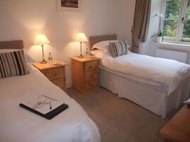 A bedroom with two beds, bedside tables with lamps, a window with curtains, and a radiator.
