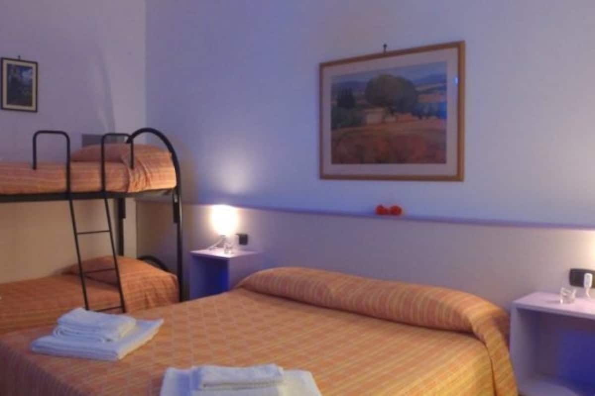 Una habitación con literas, dos mesitas de noche con lámparas, y un cuadro en la pared.
