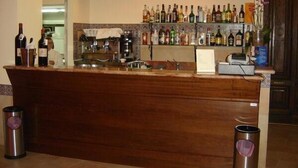 Un espace bar avec un comptoir en bois, diverses bouteilles d’alcool, un appareil à café et un téléviseur fixé au-dessus du comptoir.